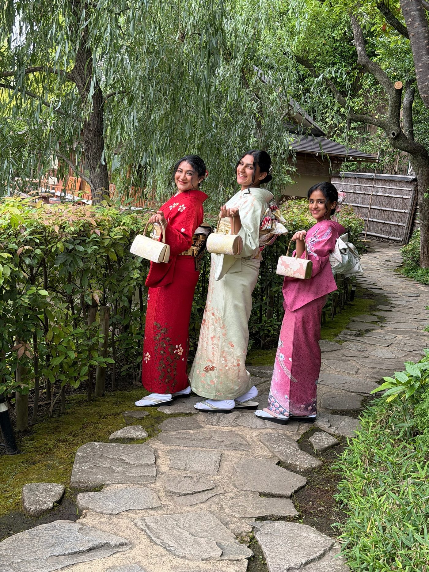 The daughters and their mother in kimono on a stone path in a Kyoto garden