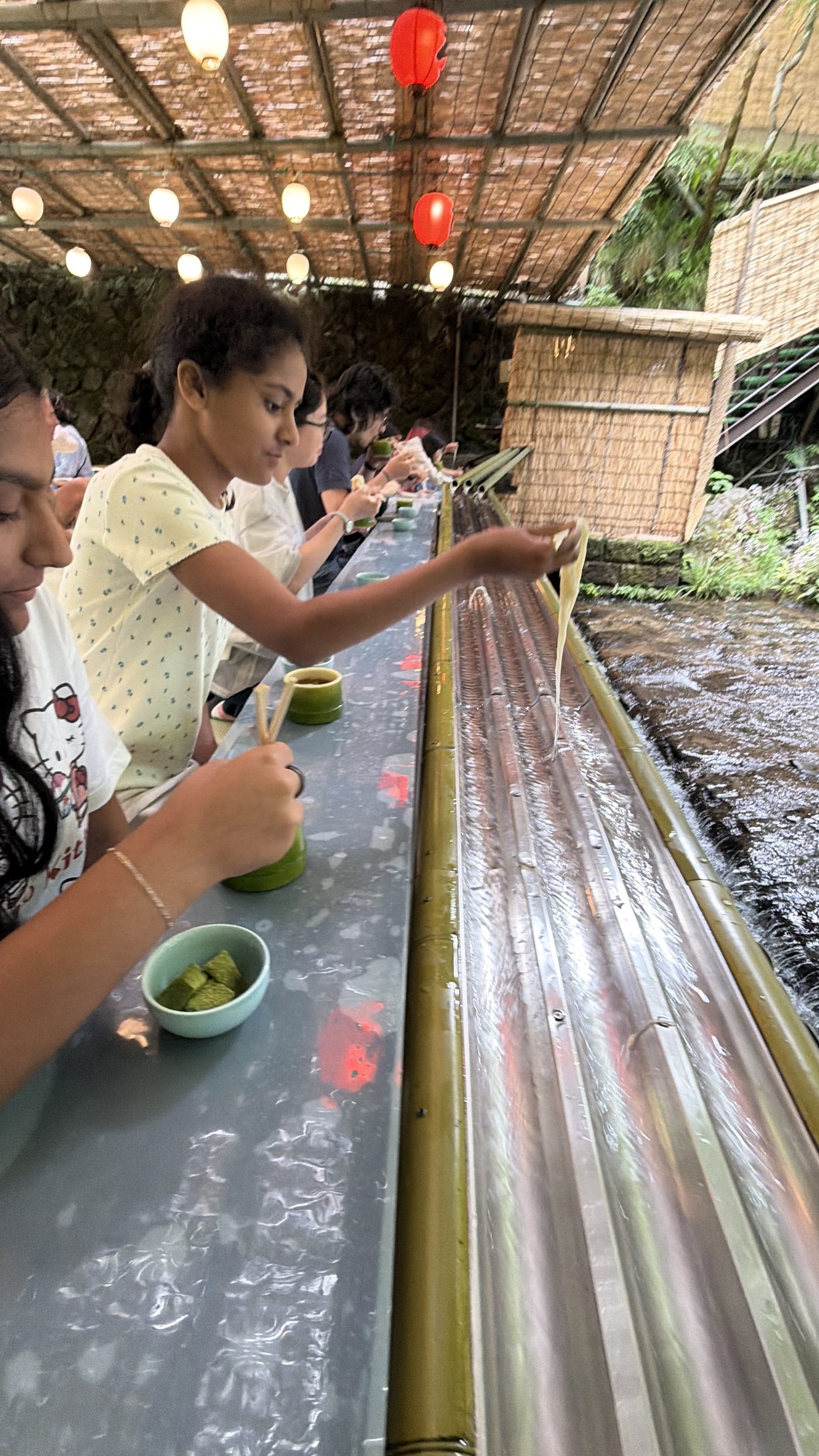 The daughters catching flowing somen noodles from a split-bamboo flume